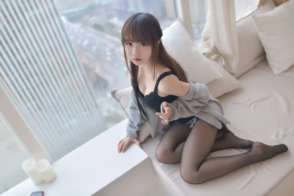 落地窗旁白床上伸手望向镜头的灰衣长发女子