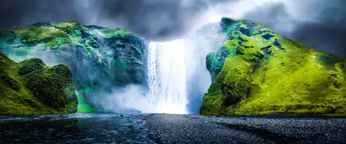 3840x1600 Ultrawide 自然风景 Wallpaper - 乌云下苔绿峭壁间的宽阔瀑布与黑色砾石滩